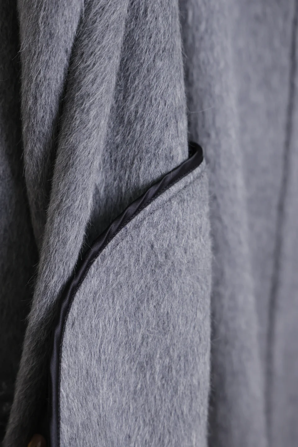 Close view of grey coat fabric and a pocket opening with a dark edge.